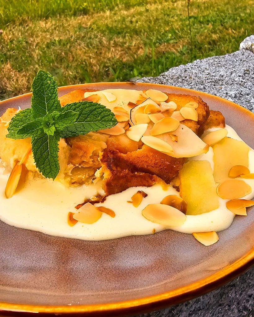 Nahaufnahme einer Portion warmem Ofenschlupfer mit Vanillesoße, die dampfend aus dem Omnia Campingbackofen serviert wird.