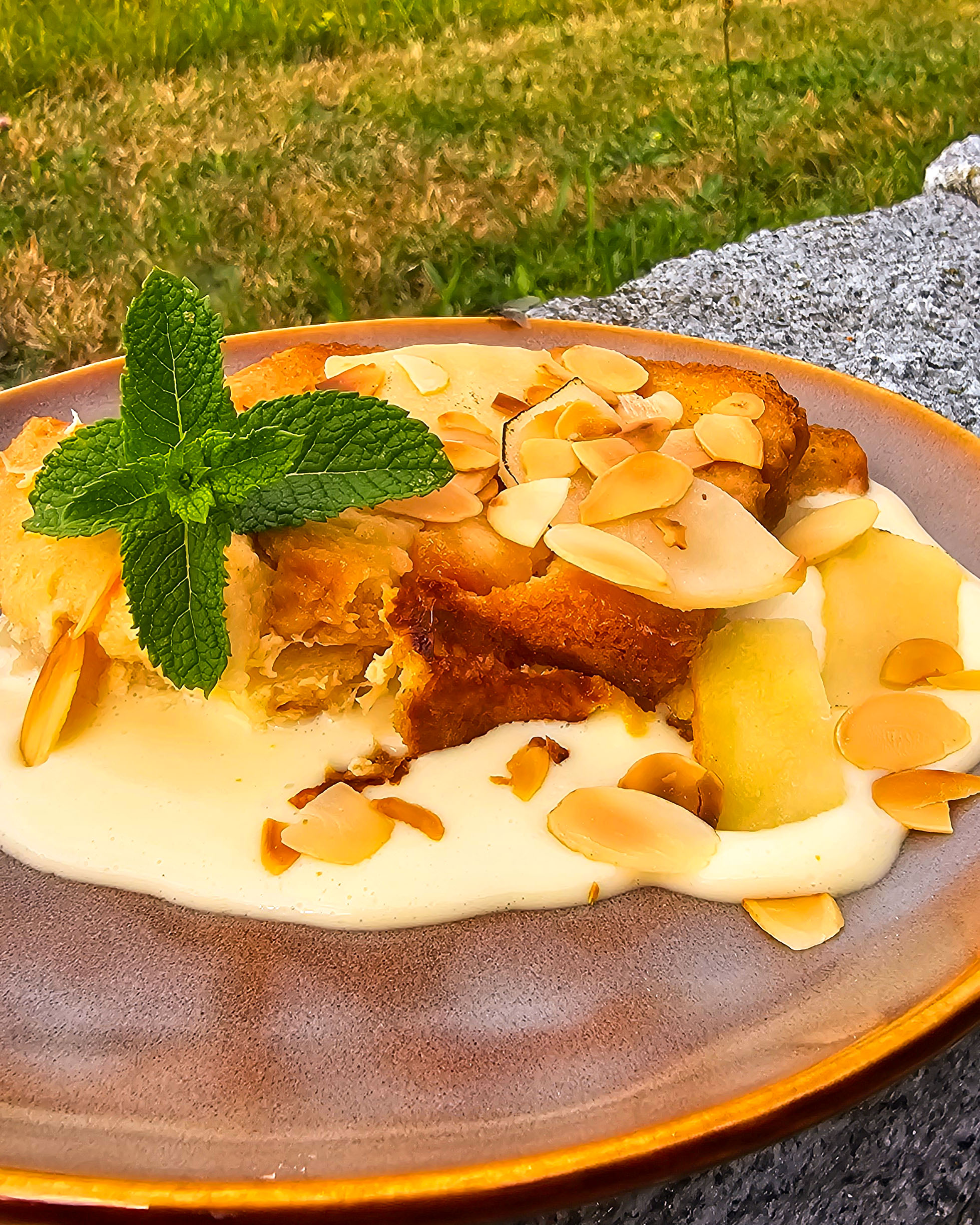 Nahaufnahme einer Portion warmem Ofenschlupfer mit Vanillesoße, die dampfend aus dem Omnia Campingbackofen serviert wird.