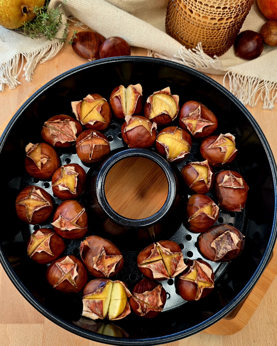 Geröstete Maronen in der Omnia-Backform, die gerade frisch aus dem Campingbackofen genommen werden, auf einem rustikalen Holztisch