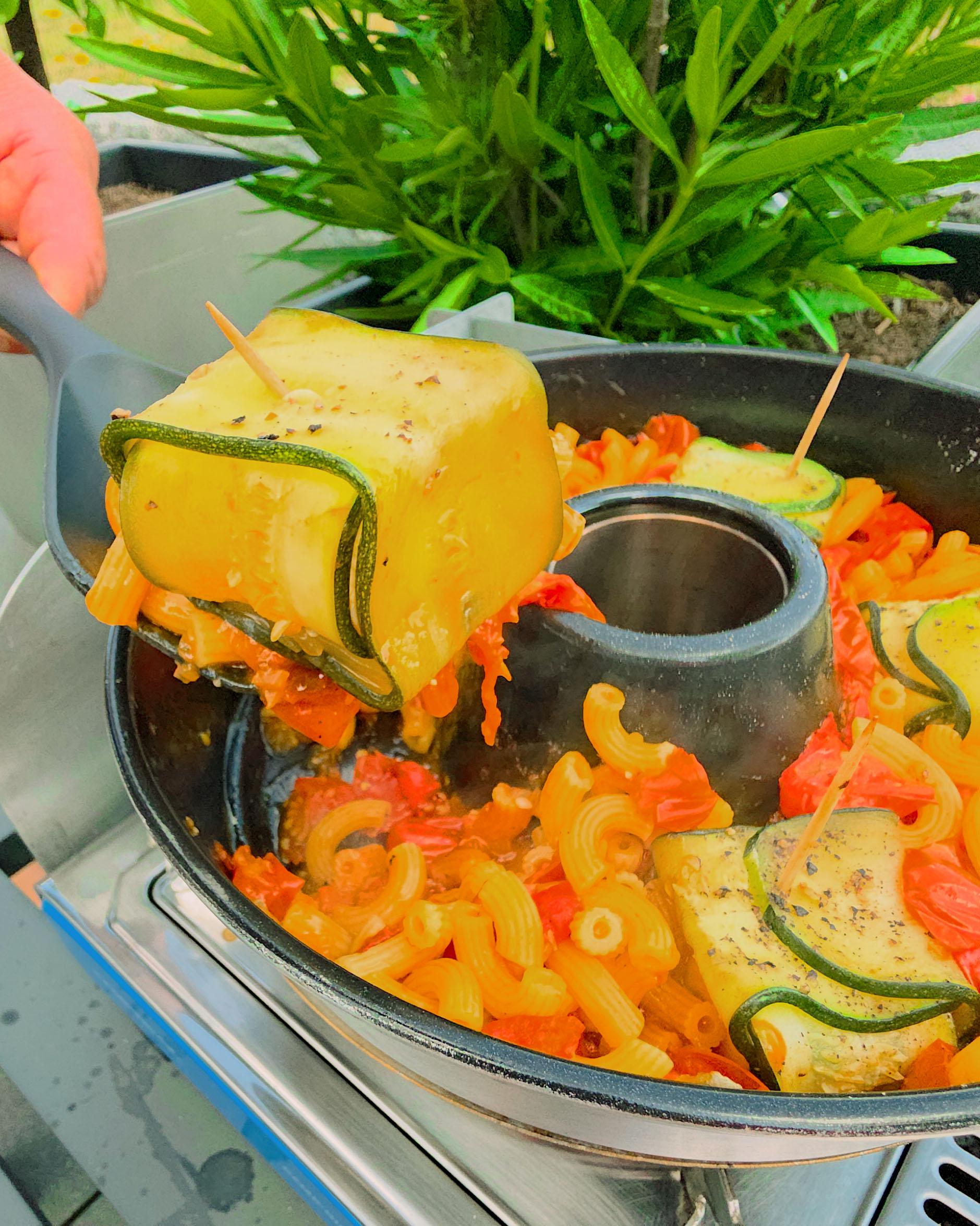 Zucchini-Feta-Päckchen auf einem Bett aus Pasta mit frischen Tomaten im Omnia Campingbackofen.