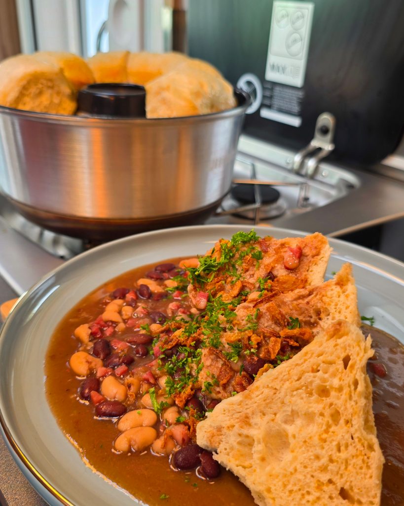 Goldbraun gebackene Hefeknöpfle in der runden Omnia Backform, serviert auf einem Teller neben einer Portion Bohnenkerne (Speck-Bohnen)