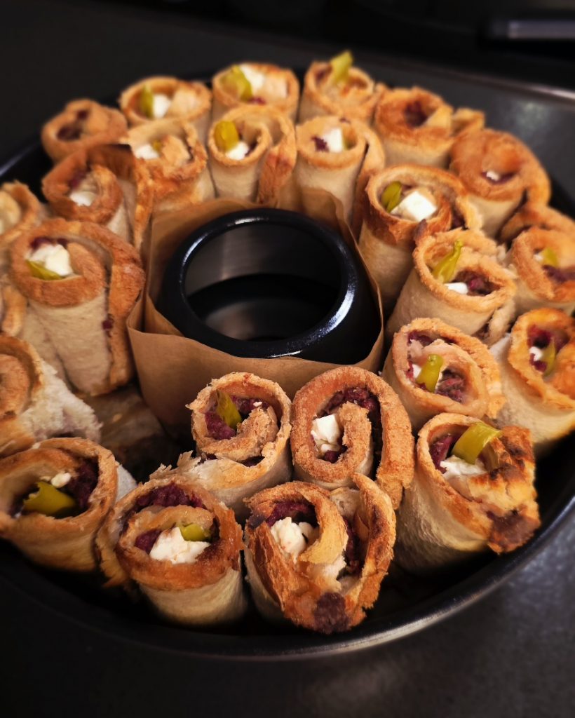 Goldbraun getoastete Toast-Röllchen mit Dönerfleisch, Feta und Peperoni-Füllung im Omnia Campingbackofen.