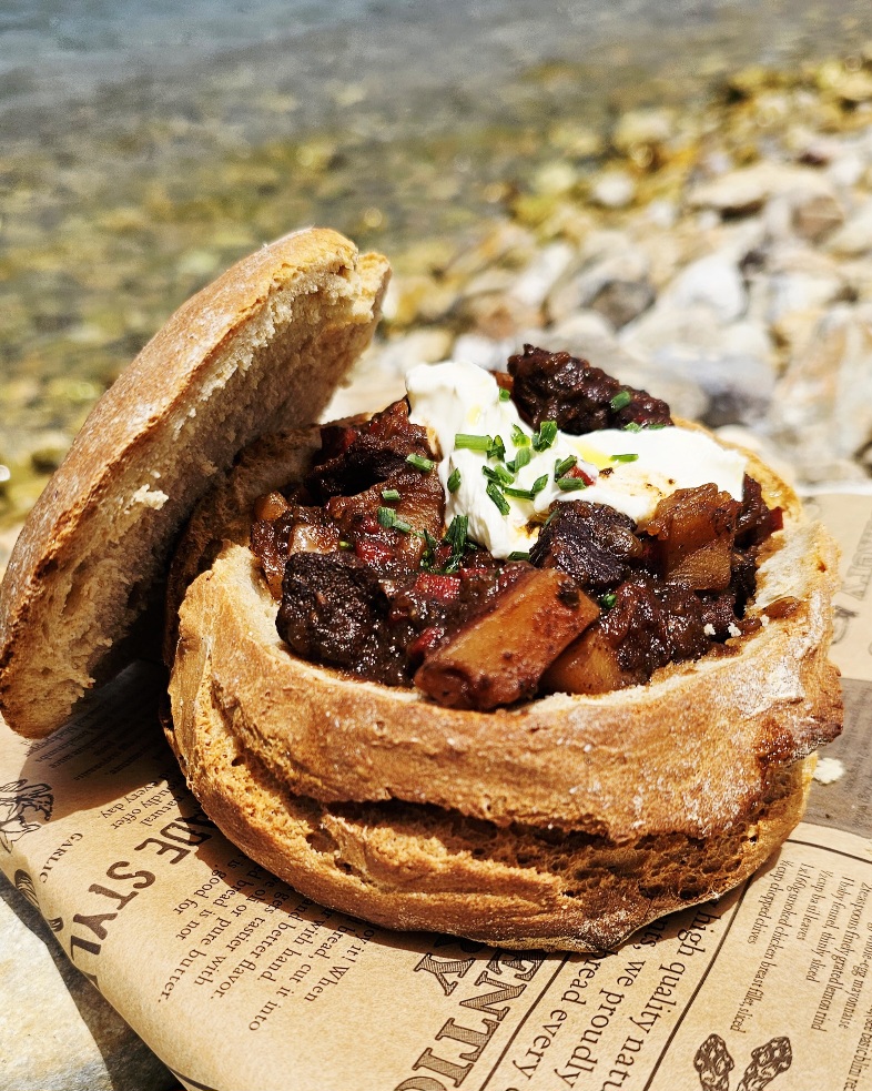 gulasch-im-brot-big-green-egg-minimax.jpg Deftiges Rindergulasch serviert in einem ausgehöhlten Brotlaib, frisch zubereitet auf dem Big Green Egg MiniMax Keramikgrill.