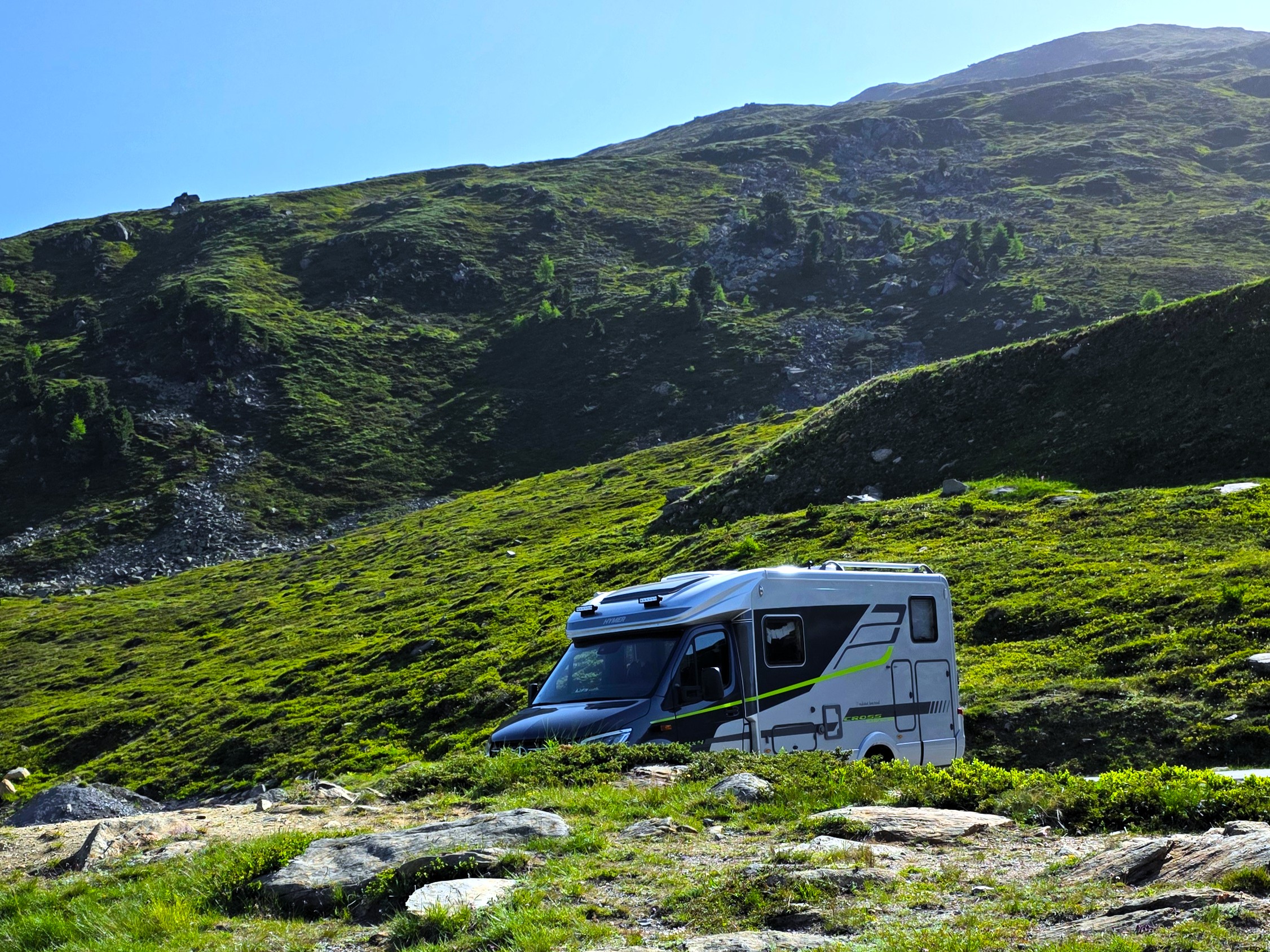 Wohnmobil fährt durch enge Serpentinen der Timmelsjoch Hochalpenstraße mit Blick auf schneebedeckte Gipfel.