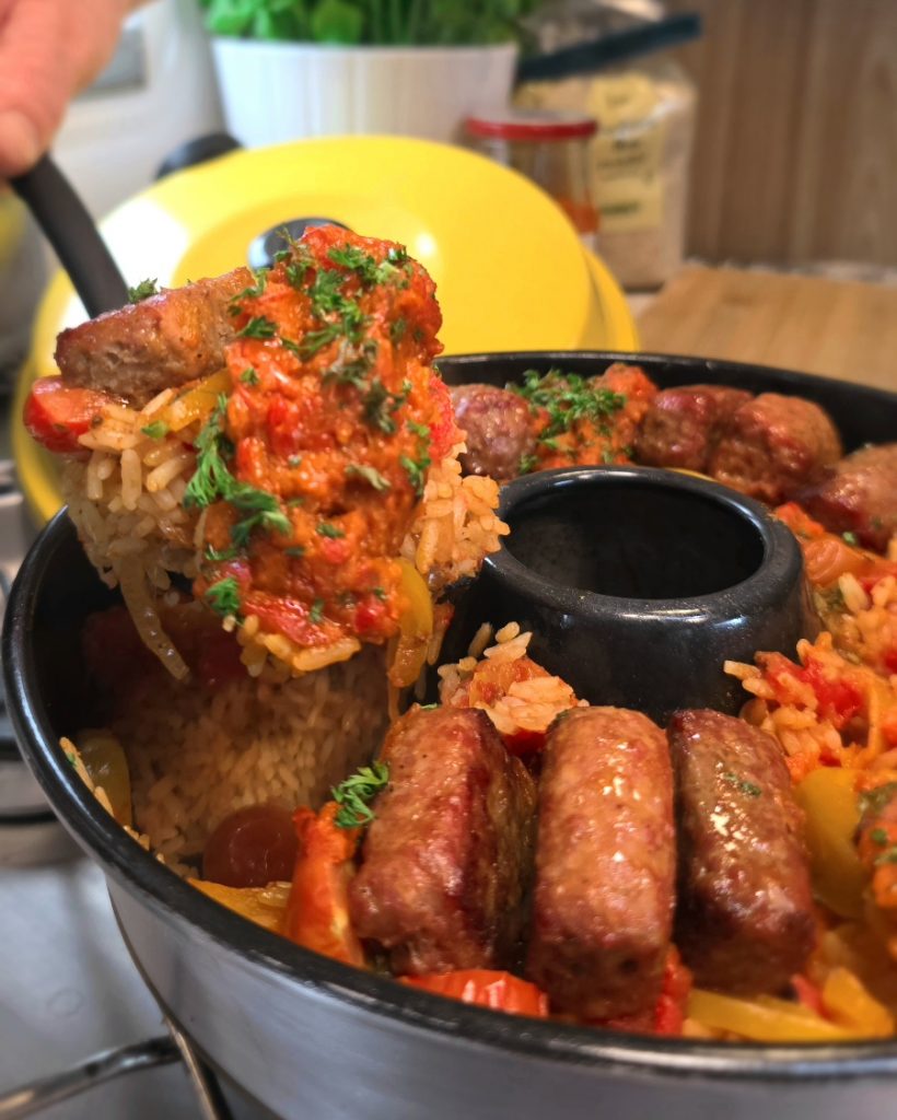 Würzig-roter Djuvec-Reis mit Ajvar und krossen Cevapcici im Omnia Campingbackofen serviert.