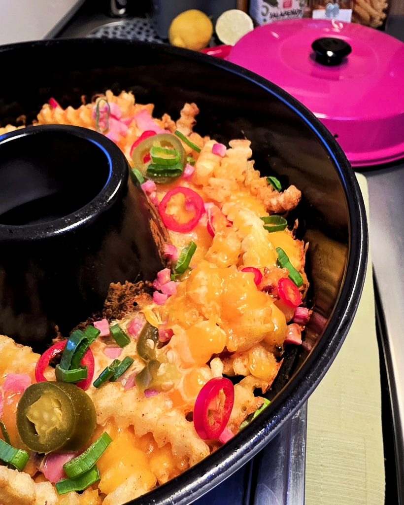 Goldgelbe Pommes in der Omnia Form, dick mit geschmolzenem Käse und Speckwürfeln überbacken.