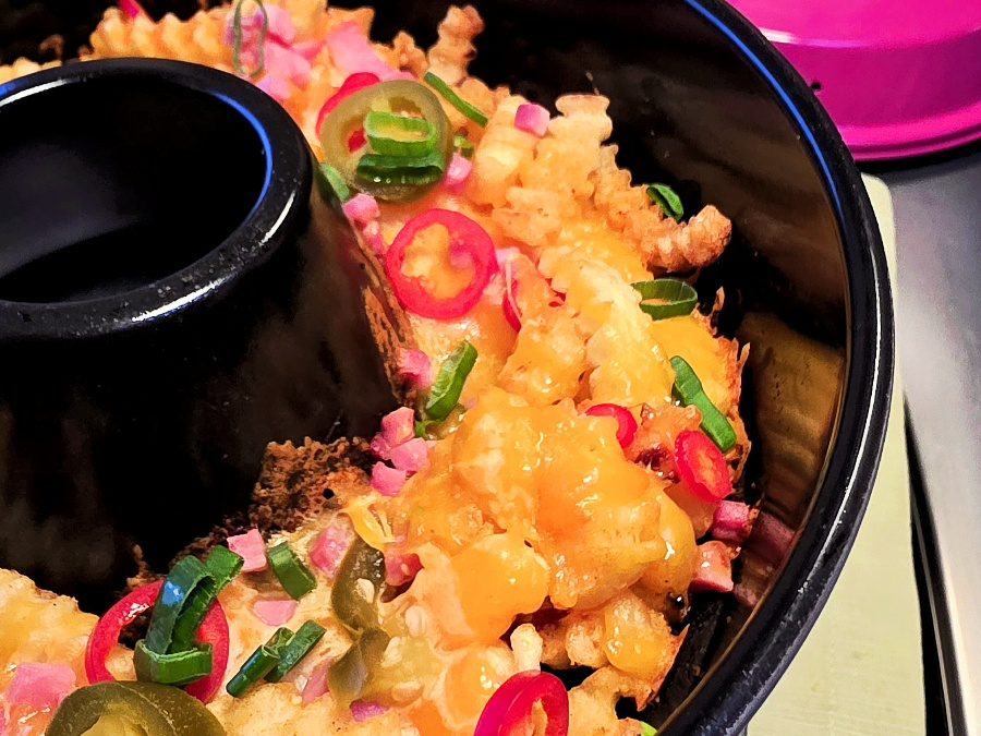 Goldgelbe Pommes in der Omnia Form, dick mit geschmolzenem Käse und Speckwürfeln überbacken.