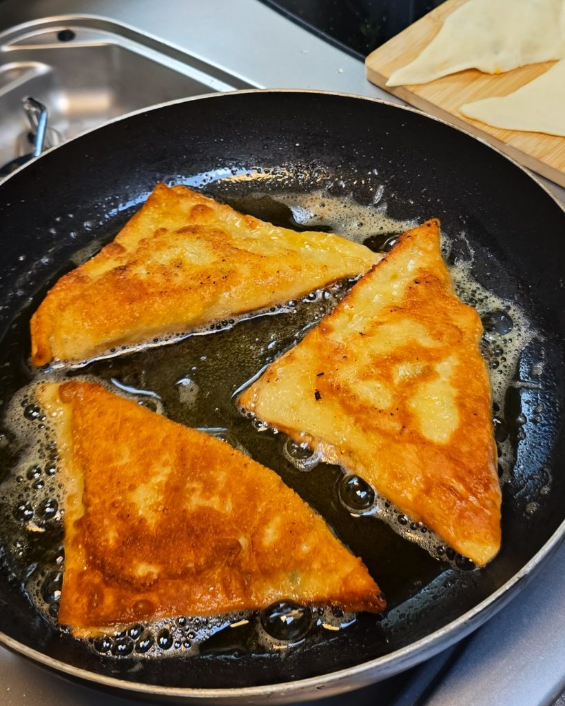 Goldbraun gebratene Flammkuchentaschen mit Speck und Zwiebeln in einer Campingpfanne auf dem Gaskocher.