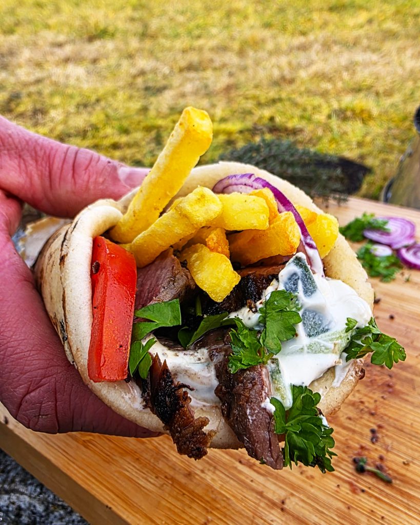 flank-steak-pita-pommes-grillrezept Gegrillte Flank Steak Streifen in einer Pita-Tasche mit Pommes frites und Tzatziki auf dem Grill serviert.