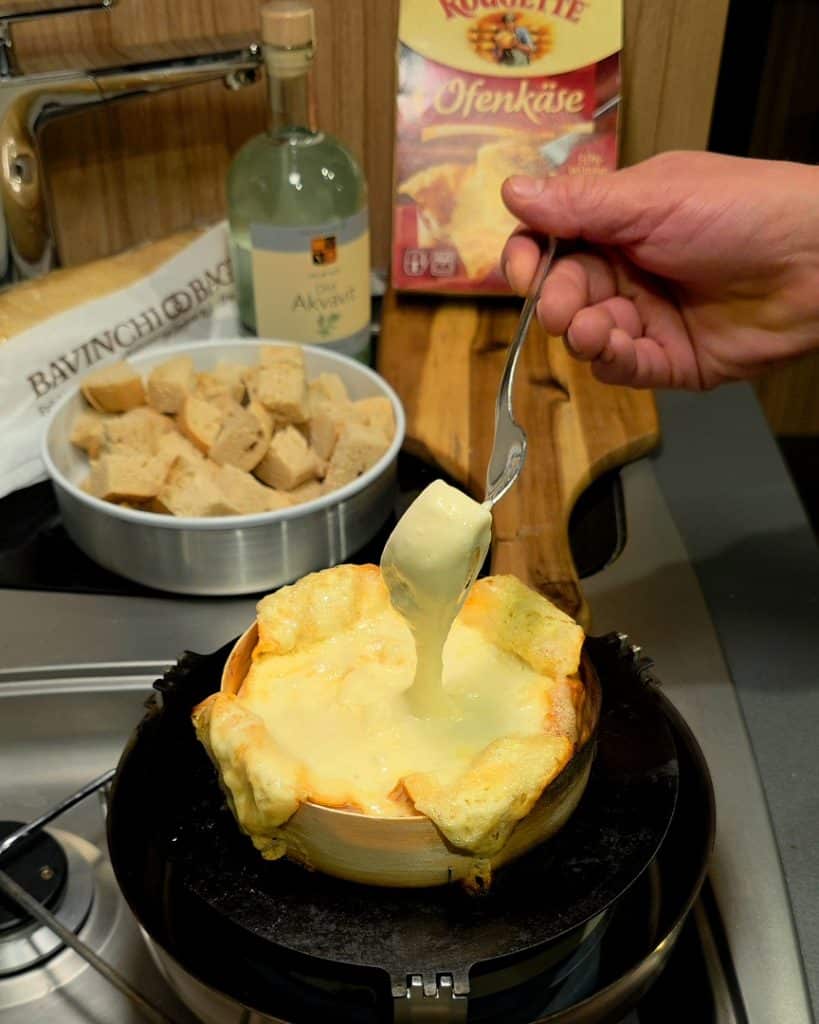 Cremig geschmolzener Ofenkäse in einer Holzschachtel auf dem Backblech im Hajka Outdoor Oven.