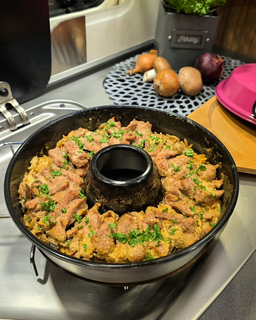 Herzhaftes Geschnetzeltes mit Orzo-Nudeln in der Omnia-Form auf einem Camping-Gaskocher.